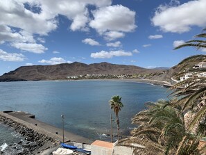 A coastal view with a clear sky, calm sea, and a mountainous backdrop.
