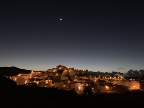 A nighttime view of a coastal town with illuminated buildings and a crescent moon in the sky.