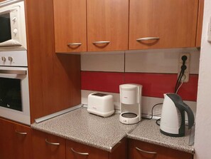 Eine kleine Küche mit Holzausstattung, Backofen, Toaster, Kaffeemaschine und Wasserkocher.
