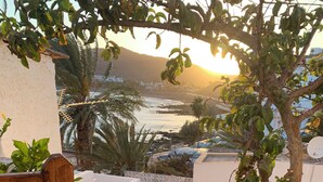 A wicker chair on a wooden deck with a view of a beach and palm trees. - Ocean View Apartment Casa Las Playitas – Terrace – 1 Minute to the Beach (Las Playitas)