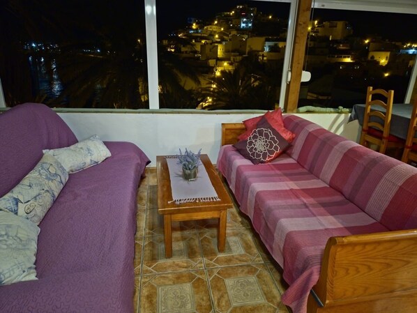 A room with two sofas, a small table with a vase, and a view of a cityscape at night.