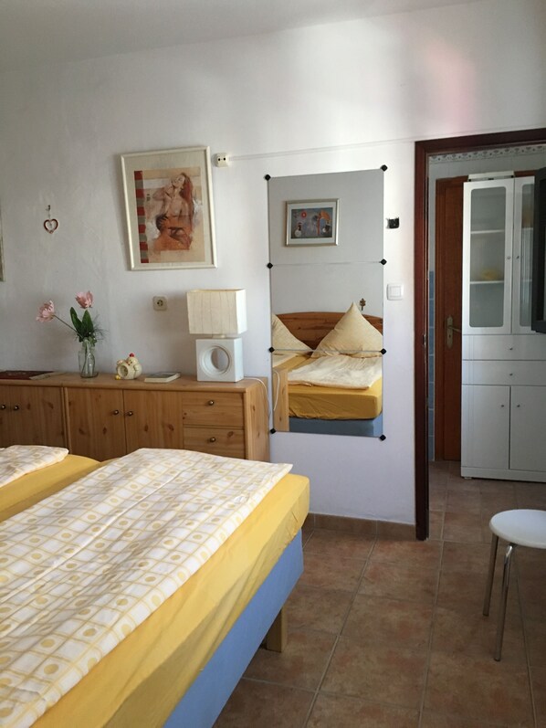 A bedroom with two beds, a wooden dresser, a bedside table with a lamp, and a small cabinet.