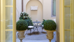 Une terrasse extérieure avec une table ronde et deux chaises, entourée de plantes en pot et d’un mur décoratif.