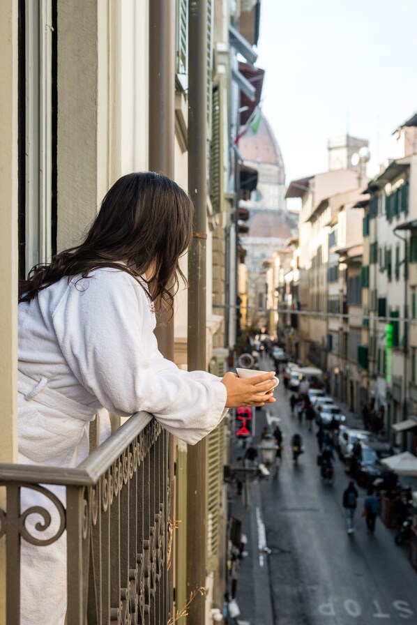 A person leaning on a balcony railing overlooking a street with buildings and shops.