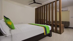 Un dormitorio con cama, ventilador de techo, separador de madera y un sofá al fondo.