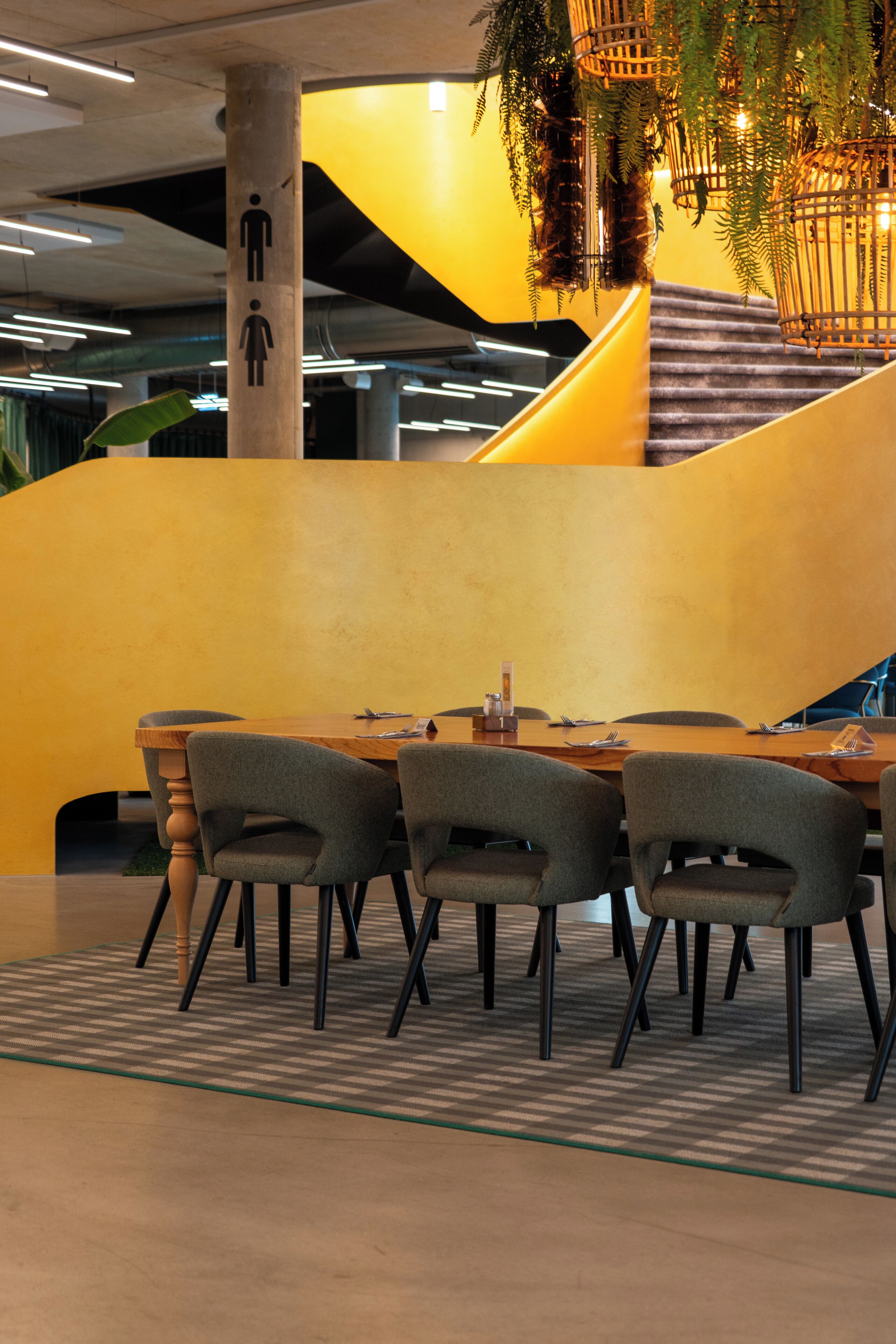A modern interior with a wooden table and chairs, a staircase, and a yellow accent wall.