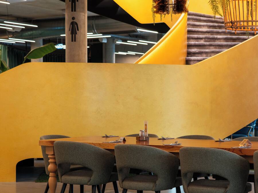 Un intérieur moderne avec une table et des chaises en bois, un escalier et un mur d’accent jaune.