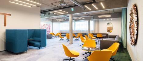 A modern office space with teal and yellow chairs, a large table, and a view of the city through large windows.