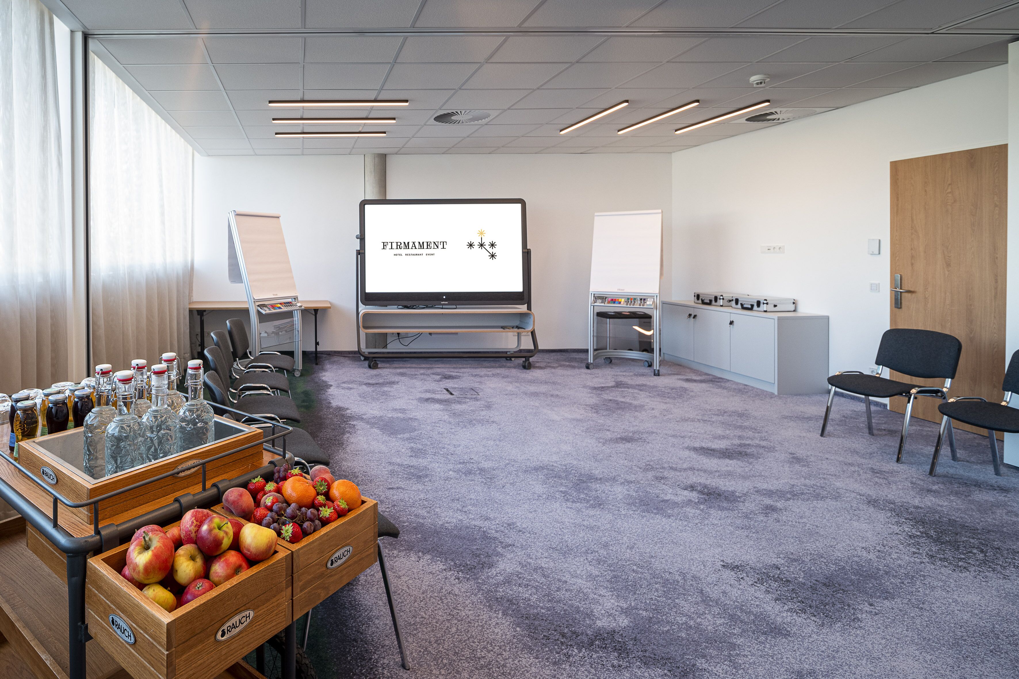 Una sala conferenze con uno schermo per presentazioni, un buffet di frutta e una lavagna.