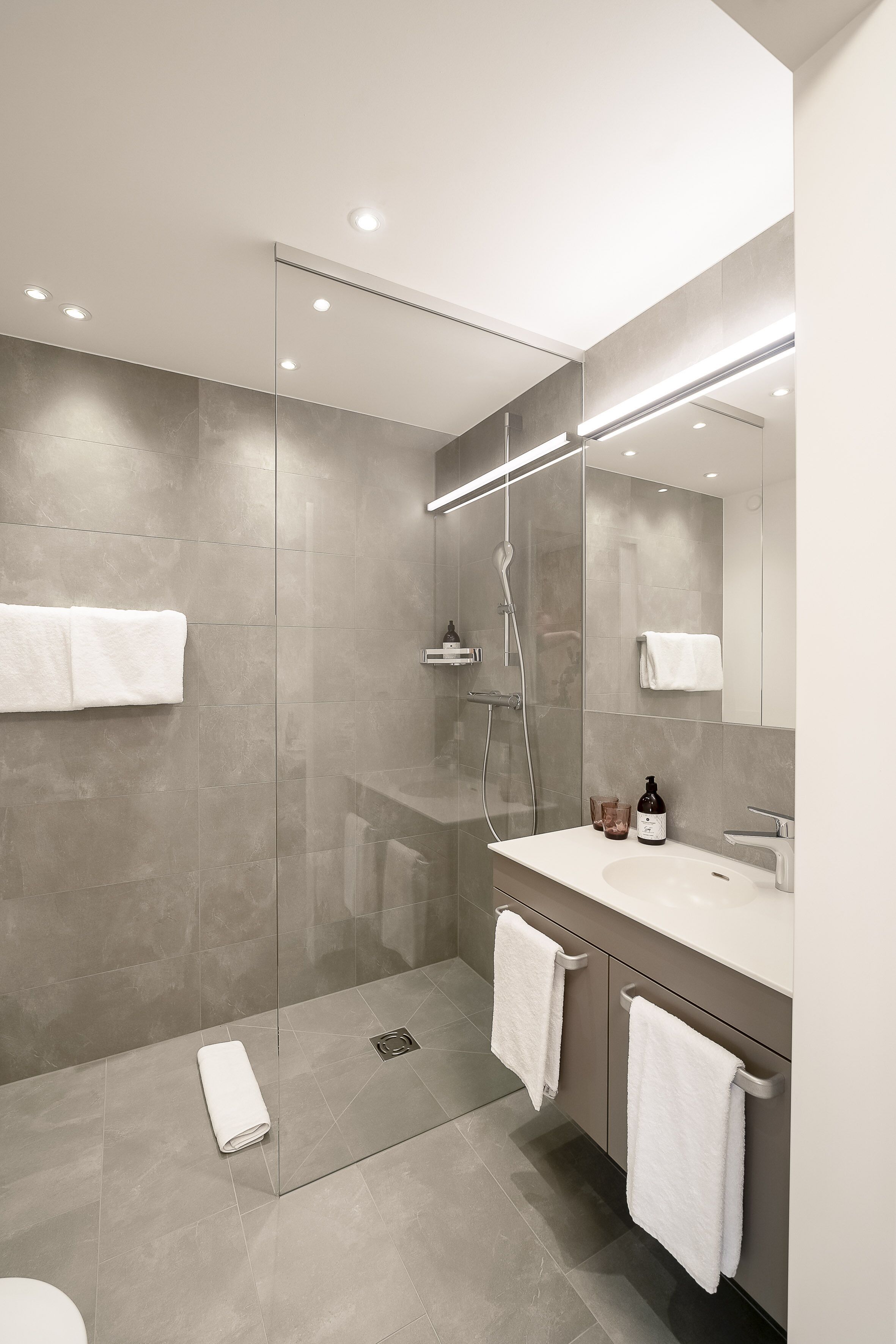 Un baño moderno con ducha envuelta en vidrio, un espejo grande y un lavamanos blanco.