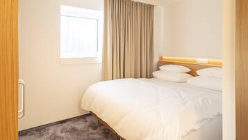 Habitación de hotel con una cama grande, una ventana con cortinas, una lámpara en el techo y piso alfombrado.