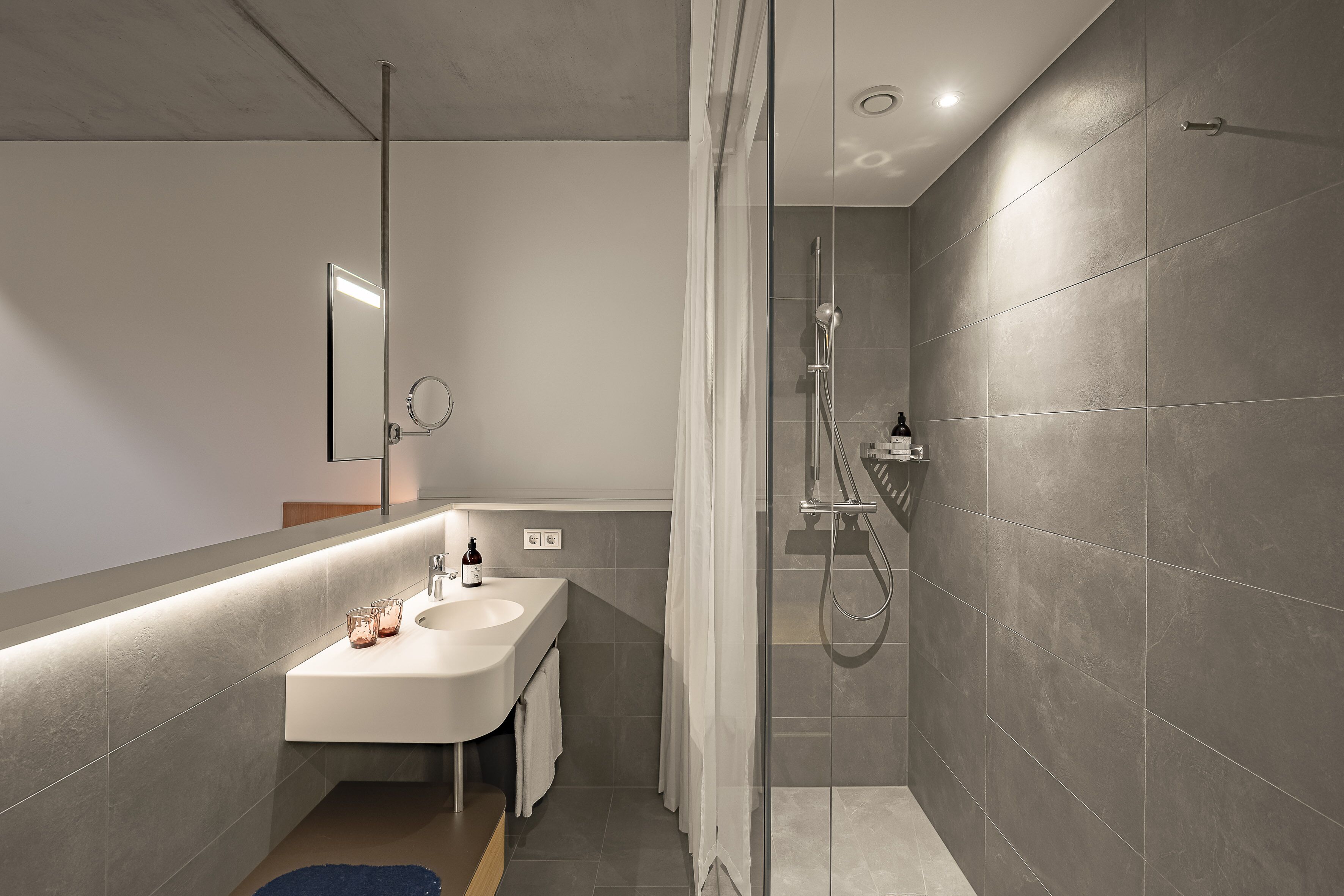 Une salle de bain moderne avec un lavabo blanc, un miroir et un espace douche.