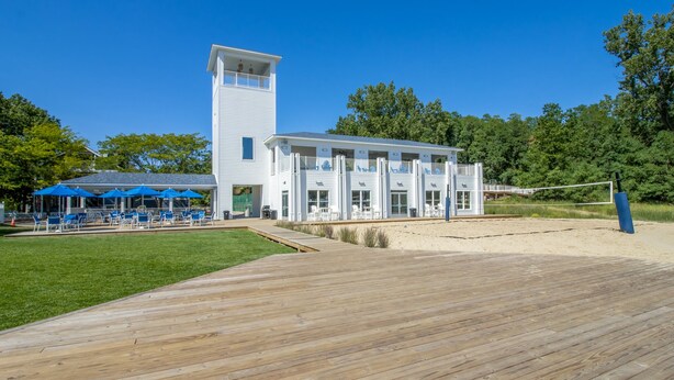 Un hotel al costat de la platja amb terrassa de fusta, mobiliari exterior i una torre alta.