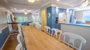 A spacious kitchen with a long wooden table and white chairs, blue cabinets, and a ceiling fan. - Massive Beachwalk Resort Home with Lake Views (Michigan City)