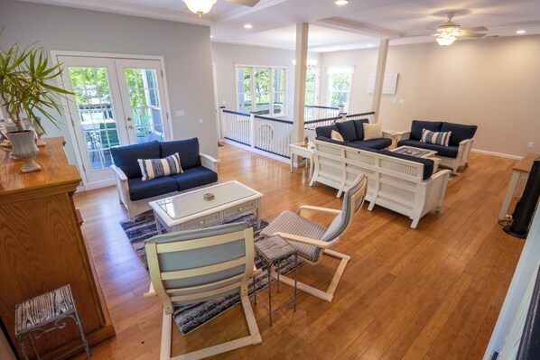 A spacious living area with a wooden floor, a blue sofa set, a white armchair, and a small table. - Massive Beachwalk Resort Home with Lake Views (Michigan City)