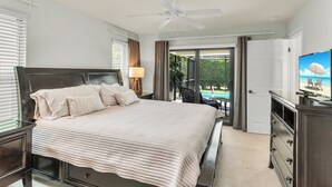 A bedroom with a bed, a ceiling fan, a TV, and a view of the outdoors. - Short Walk to Maple Beach Access I 3/2 w/ Heated Pool (Marco Island)