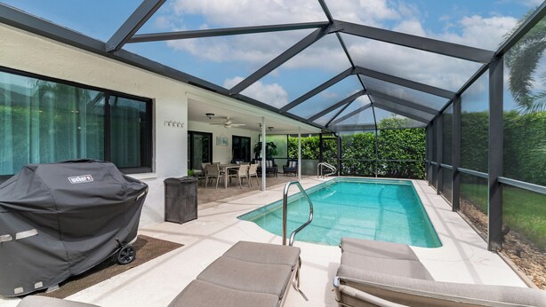 A covered outdoor pool area with lounge chairs, a barbecue grill, and a patio table. - Short Walk to Maple Beach Access I 3/2 w/ Heated Pool (Marco Island)