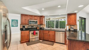 A modern kitchen with wooden cabinets, stainless steel appliances, and a large window providing natural light. - Short Walk to Maple Beach Access I 3/2 w/ Heated Pool (Marco Island)