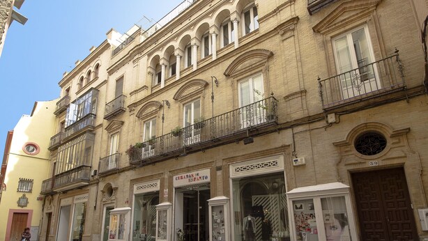 Un immeuble à plusieurs étages dont le rez-de-chaussée est occupé par des boutiques, notamment un magasin dont l’enseigne indique : « CURADAS DE ESPANTO ».