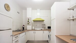 Une cuisine compacte avec des meubles blancs, un évier, un four à micro-ondes et un lave-linge.