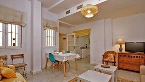 Un salon avec un canapé, une table à manger entourée de chaises, un téléviseur et, au fond, une cuisine.