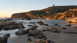 Una playa rocosa con grandes rocas y un castillo en una colina al fondo.