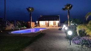 Una casa con piscina, patio y jardín con palmeras.