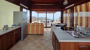 Una cocina con techo de madera, un refrigerador, un comedor con mesa y sillas, y vistas al exterior.