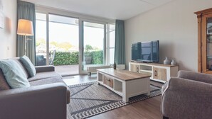 A modern living room with a sofa, coffee table, TV, and a view of the outdoors through large windows.