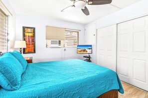 A bedroom with a bed, a ceiling fan, a window with blinds, a TV, and a door.