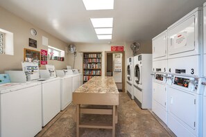 A laundry room with multiple washing machines, a table, and a bookshelf.