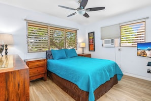 A bedroom with a bed, wooden nightstands, a ceiling fan, and windows with blinds.