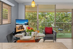 A dining area with a glass table, chairs, and a TV displaying a beach scene.