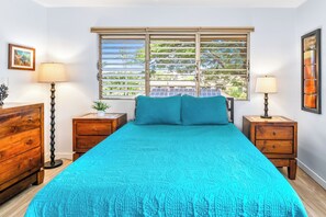 A bedroom with a large bed, two nightstands, a wooden dresser, and a window with blinds.
