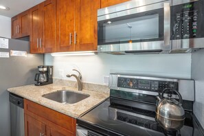 A modern kitchen with wooden cabinets, a stainless steel microwave, a kettle, and a dishwasher.
