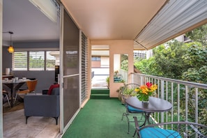 A balcony with a green artificial turf, a dining area with a table and chairs, and a flower vase.