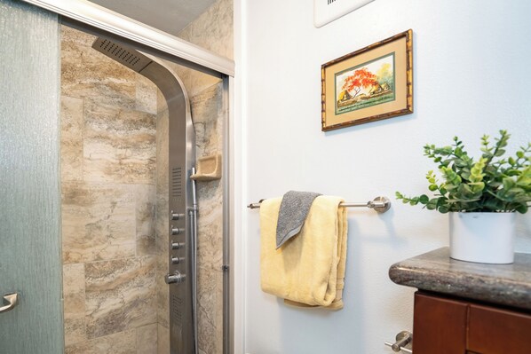 A bathroom with a shower, a towel rack, a framed picture on the wall, and a potted plant on the counter.