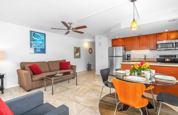 A modern living room with a brown sofa, a coffee table, and a dining area with orange chairs and a glass table.