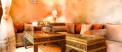 A cozy living room with a sofa, two ornate coffee tables, a lamp, and a patterned rug.