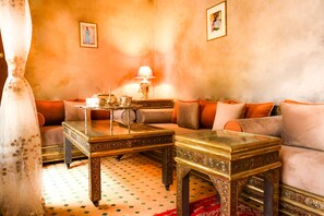 A cozy living room with a sofa, two ornate coffee tables, a lamp, and a patterned rug.