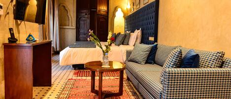 A hotel room with a bed, a sofa, a small table with a vase, and a decorative wall.