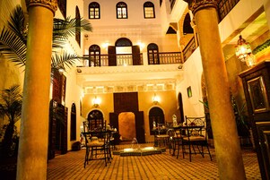 Un patio con suelo de baldosas, palmeras y una zona de estar con mesas y sillas.