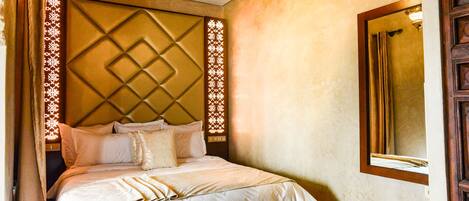 A hotel room with a large bed, a headboard with a diamond pattern, and a mirror on the wall.