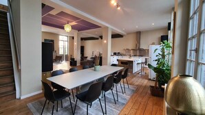 Eine moderne Küche mit einer zentralen Kochinsel, einem Essbereich mit großem Tisch und Stühlen sowie ein Wohnbereich mit Sofa und Fernseher.
