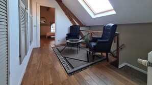 Ein Schlafzimmer im Loft-Stil mit Dachfenster, Holzbalken, einem Bett, zwei Stühlen und einem kleinen Tisch.
