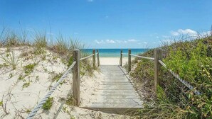 A wooden boardwalk leading to a sandy beach with a clear blue sky.