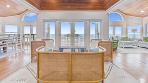 A spacious living area with wicker furniture, large windows, and a wooden ceiling.