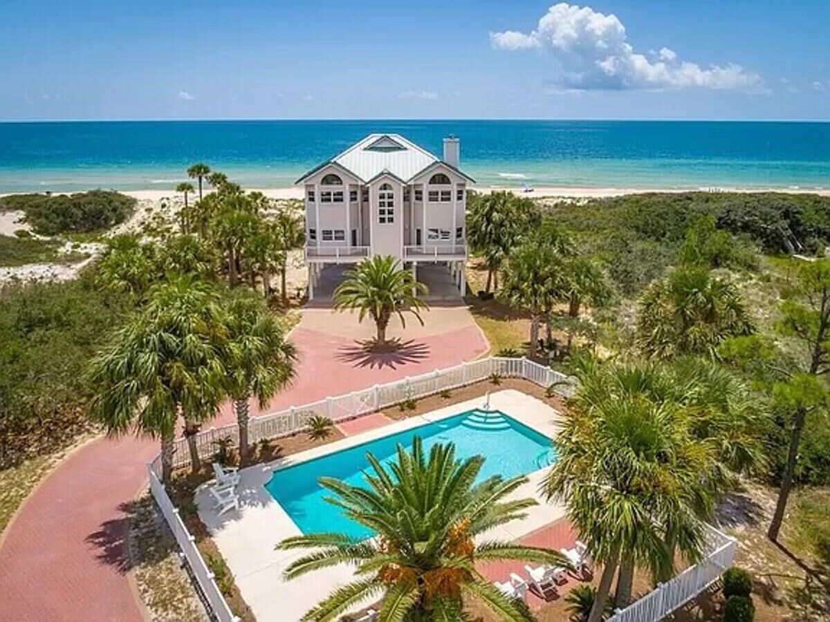 Ein großes Haus mit Swimmingpool, umgeben von Palmen und Blick auf den Strand.