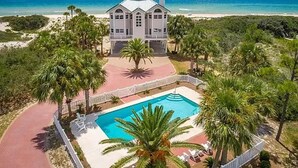 A large house with a swimming pool, surrounded by palm trees and a beach view.