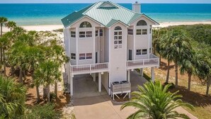 A two-story beachfront house with a green roof, multiple balconies, and a view of the ocean.
